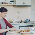 Young mother rolling dough and talking to her little cute daughter while cooking in the kitchen on weekend. Family, food, home and people concept