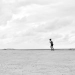 A lone runner on a vast, open terrain under a cloudy sky, captured in Natal, Brazil.