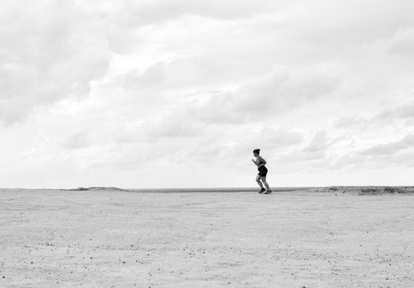 A lone runner on a vast, open terrain under a cloudy sky, captured in Natal, Brazil.